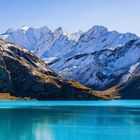 Schneebedeckte Berge umrahmen einen türkisfarbenen See unter klarem, blauem Himmel.