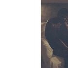 Keine Texte erkennbar. Ein Mensch sitzt nachdenklich auf einem Bett in einem dunklen Raum.