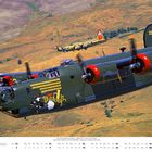„Witchcraft“ steht in gelber Schrift auf einem grünen Flugzeug. Majestätische Hügel im Hintergrund. Kalender für Mai.
