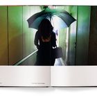 Texte: "Above Lime Previous Crossing". Person mit Regenschirm in einem schmalen, grün beleuchteten Gang von hinten gesehen.