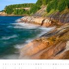 Pictured Rocks National Lakeshore, Michigan. Wellen schlagen gegen bunte Felsen unter einem klaren blauen Himmel. März-Kalender.