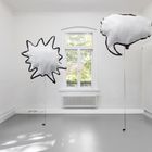 Zwei Sprechblasen-Illustrationen schweben in einem leeren, weißen Raum mit Fenster.