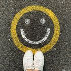 Weiße Turnschuhe und Jeans stehen auf Asphalt mit gelb-weißem Smiley.
