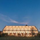 Text: "125 Halle communale à Ancy-sur-Moselle." Ein beleuchtetes Gebäude mit einem transparenten, modernen Dach bei Abenddämmerung.