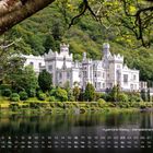 Kylemore Abbey - Benediktinerinnenabtei, Kalender unten, Schloss mit Türmen und Garten, umgeben von Bäumen und See.