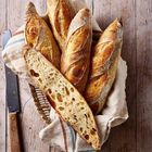 Knusprige Baguettes in einem Korb auf einem Tuch, ein Brotmesser daneben, rustikale Holzhintergrund.