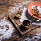 Serviettenlogo: Somberg. Teller mit Kaiserschmarrn, Puderzucker, Apfelmus, Marmelade. Holzbrett. Mehlherz auf Tisch.