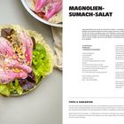 "Magnolien-Sumach-Salat", Rezeptbeschreibung und Zutatenliste. Auf einem Teller liegen rosa-weiße Blätter über Salat.