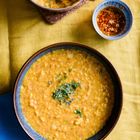 Schüssel mit gelbem Linsengericht, garniert mit Kräutern. Daneben eine kleine Schüssel mit gerösteten Gewürzen.