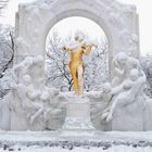 „Johann Strauss“ steht auf einem Sockel. Eine goldene Skulptur zeigt einen Geiger, umgeben von Figuren in einem verschneiten Park.