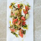 Das Gericht zeigt einen gegrillten Gemüseaufschnitt mit Joghurt, Grapefruitstücken, Kräutern und Olivenöl auf Papier.