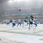 28 - 22 (W), RAMS, WK 20. Ein Football-Spiel im Schnee. Spieler rennen, ein Team trägt grüne, das andere blaue Uniformen.