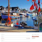 November 2027, 46. Woche, Buß- und Bettag: 17. Hafenansicht mit Booten und roten Fahnen, blauem Himmel, Gebäude im Hintergrund.