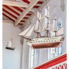 Text: "49 DEZEMBER MO 06 DI 07 MI 08..." zeigt einen Kalender. Modellschiff hängt in Kirche, Decke rot-weiß, Dachgebälk sichtbar.