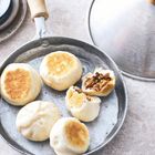 Bratpfanne mit fünf gedämpften Brötchen, eines aufgeschnitten mit sichtbarer Füllung, daneben ein abgenommenes Deckel.