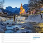50. Woche, Dezember 2027. Kirche in winterlicher Landschaft, Bach und Brücke im Vordergrund, verschneite Berge im Hintergrund.