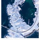 19 So, 50. Woche 2027, DEZEMBER. Fischerort, verschneite Küste mit Gebäuden, Straßen, grünes Wasser, Boote.