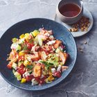 Ein blauer Teller mit buntem Gemüse, Lachs und Hüttenkäse. Daneben ein Schälchen mit Dressing und ein paar Pinienkernen.