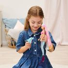 Ein Mädchen in einem blauen Kleid spielt mit einer Barbiepuppe und einem kleinen Spielzeugdelfin. Im Hintergrund ein Regal.