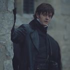 Keine sichtbaren Texte. Ein Mann in dunkler Kleidung lehnt an einer Steinwand und schaut zur Seite.