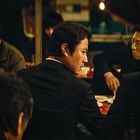 Eine Gruppe von Männern in Anzügen sitzt zusammen in einer dunklen, gemütlichen Atmosphäre.