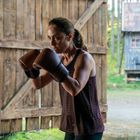 Eine Frau mit braunen Boxhandschuhen trainiert intensiv an einem Boxsack in einem rustikalen Raum.