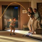 Ein Kind steht spielerisch gespannt, während ein Plüschtier mit langem Schwanz in Richtung eines Erwachsenen schwingt.