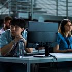 Personen an Computern in einem modernen Raum, konzentriert bei der Arbeit. Im Vordergrund eine Wasserflasche.