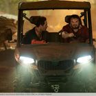 Zwei Männer sitzen in einem Geländefahrzeug, der Fahrer schaut entschlossen, der Beifahrer überrascht zur Seite.