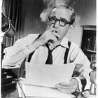 SBA-PUB-61. Ein Mann mit Brille und Hemd sitzt an einem Schreibtisch, hält Papiere und raucht. Im Hintergrund Bücherregal.