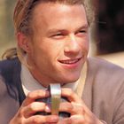 Ein Mann mit langen Haaren lächelt, während er einen Metallbecher in beiden Händen hält.