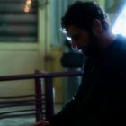 Ein Mann sitzt nachdenklich mit gesenktem Kopf neben einem hell erleuchteten Automaten in einem dunklen Raum.