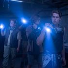 Drei Personen mit Taschenlampen in einem dunklen Raum, tragen Schutzmasken um den Hals.