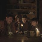 Fünf Personen sitzen an einem Tisch in einem warm beleuchteten Raum. Sie schauen neugierig auf ein kleines Feuer.