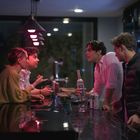 Menschen in einer Bar, die sich unterhalten. Eine Person hält eine Flasche mit der Aufschrift „Clean Vodka“.