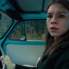 Eine Frau mit erschrockenem Ausdruck sitzt in einem blauen Oldtimer vor einer bewaldeten Kulisse.