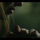 Kein Text erkennbar. Nahaufnahme eines nachdenklichen Gesichts mit Händen, die Kinn und Lippen berühren. Stimmungsvoll, gedämpftes Licht.