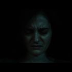 Eine Frau mit geschlossenen Augen und ernstem Gesichtsausdruck in dunkler Umgebung.