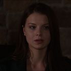 Eine Frau mit langen braunen Haaren schaut ernst; Hintergrund aus Steinwand.