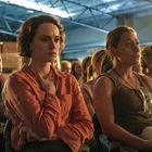 Menschen sitzen in einem Raum, scheinbar aufmerksam. Die Beleuchtung ist warm und von oben.