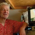 Text auf dem Monitor: "Peng! Du bist hypnotisiert!" Daneben ein lächelnder Mann in rotem Hemd. Technikraum.