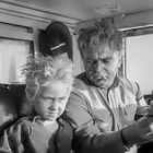 Zwei Personen im Inneren eines Fahrzeugs, ein Mädchen mit wilder Frisur und ein Mann, der nachdenklich schaut.