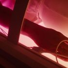 Ein Arm mit Sensor am Finger, liegend auf einer rosa-leuchtenden Fläche. Kabel sind zu sehen.