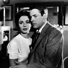 Ein Mann und eine Frau in einem Schwarz-Weiß-Raum, sorgenvoll, er im Anzug, sie im T-Shirt. Im Hintergrund ein Spiegel.