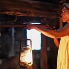 Eine Frau in einem gelben Kleid, hält ein Gewehr in einem dunklen Raum, erleuchtet von einer Laterne.