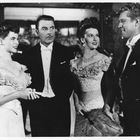 Vier elegant gekleidete Personen in Abendgarderobe lächeln und unterhalten sich in einem formellen Ambiente.