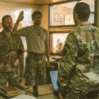 Drei Soldaten in Tarnuniform stehen in einem Raum. Zwei heben die rechte Hand zum Eid, einer der Männer steht ihnen gegenüber.