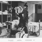 Texte: BRIGITTE BARDOT IN PLEASE, NOT NOW. Szene: Eine Frau und Mann in einem Zimmer mit Bett und Koffern.