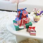 Geschenkstapel mit blauen und roten Schleifen auf einem Tisch, daneben eine Vase mit bunten Blumen.