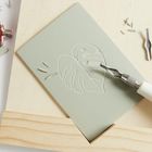 Der Text "RICO DESIGN" ist auf einem weißen Gravierwerkzeug. Eine Linolschnittplatte mit Pflanzenmotiv, daneben Werkzeuge.